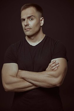 Yakışıklı kaslı bir adam kameraya bakar. Siyah arka planda stüdyo portresi. İnsanlar ve duygular. Yaşam tarzı, seçimler. Spor..