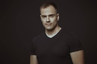 Güçlü bir adam sakince ve kendinden emin bir şekilde kameraya bakar. Siyah arka planda stüdyo portresi. Yaşam tarzı. Spor. Sporcu, vücut geliştirici..