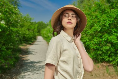 Yaz tatili. Güzel bir Asyalı genç kadın yemyeşil ve mavi gökyüzünün zeminine karşı bir yaz parkında yürüyor. Mutlu güneşli günler..