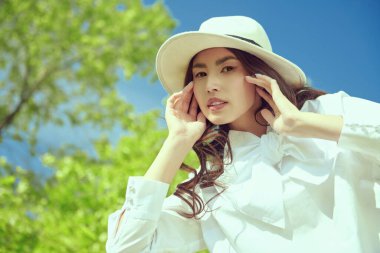 Güzel bir Asyalı genç kadın yemyeşil ve mavi gökyüzünün zeminine karşı bir yaz parkında yürüyor. Mutlu güneşli günler. Yaz tatili.