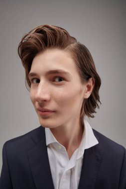 Modern eğitim. İnsanlar ve duygular. Klasik takım elbiseli, meraklı ve şaşırmış bir gencin portresi. Gri stüdyo geçmişi.