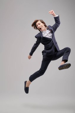 Başarı için çabalamak, büyük hırslar. Beyaz gömlekli, klasik takım elbiseli heyecanlı bir genç tüm gücüyle büyük bir sıçrama yapıyor. Gri bir arka planda tam boy portre. Modern eğitim.