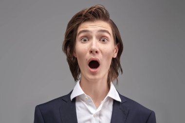 Modern eğitim. İnsanlar ve duygular. Klasik takım elbiseli bir gencin portresi, güçlü korku, sürpriz ve heyecan ifade ediyor. Gri stüdyo geçmişi.