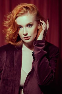 Pahalı kadife ceketli, loş ışıklı bir odada kızıl saçlı çekici bir genç kadın. Moda ve kadınlık. Kadın güzelliği ve tarzı. Oklu zarif bir makyaj. Zarif saç stili..