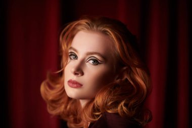 Pahalı kadife bir erkek ceketi içinde loş bir odada güzel kızıl saçlı genç bir kadının portresi. Moda ve kadınlık. Kadın güzelliği ve tarzı. Oklu zarif bir makyaj. Zarif saç stili..