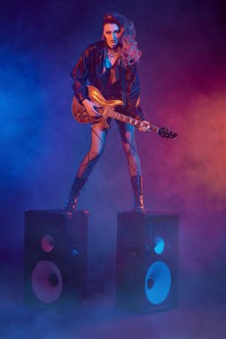 Rock konseri. Etkileyici rock yıldızı kız, müzik hoparlörlerinin üzerinde gitar çalıyor. Glam Rock tarzı.