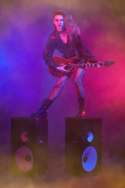 Parlak dışavurumcu müzisyen kız gitarist müzik hoparlörleri üzerinde performans sergiliyor. Glam Rock tarzı.