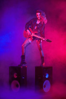 Etkileyici rock yıldızı kız, müzik hoparlörlerinin üzerinde gitar çalıyor. Rock müziği. Glam rock tarzı.