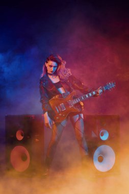 Parlak bir rock yıldızı müzisyen kız sahnede duruyor ve seyirciye gülümsüyor. Rock gitaristi, şarkıcı. Glam rock tarzı.