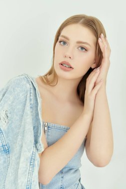 Denim Fashion. Beyaz bir stüdyo arka planında kot ceket giymiş çıplak omuzlu çekici sarışın bir kadının portresi. Kadın güzelliği.