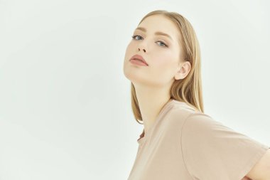 Beyaz stüdyo arka planında bej tişörtü olan güzel sarışın bir kız. İnsanların, yüzlerin ve duyguların konsepti. Metin için yer.