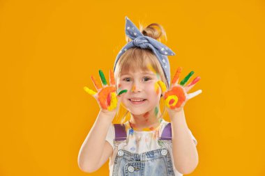 Küçük sanatçı. Renkli boyalarla boyanmış küçük tatlı bir kız, sarı bir arka planda mutlu görünüyor ve mesaj için yeri var. Çocuklar için yaratıcılık ve çizim. Çocukların hayalleri ve hayalleri.