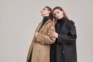 Yarı sezon modası. Beyaz stüdyo arka planında modaya uygun paltolarla poz veren iki kendine güvenen kadın manken..