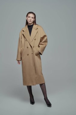 Bej renkli trençkotlu ve yüksek topuklu deri ayakkabılı şık, kendine güvenen bir kadının uzun pozu. Beyaz stüdyo geçmişi. Kadın modası.