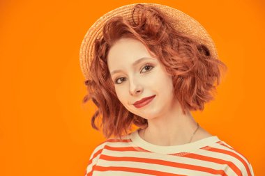 Parlak kıvırcık saçlı neşeli bir kız kameraya gülümsüyor. Turuncu stüdyo geçmişi. Mutlu hayat resimleri. Yaz havası.