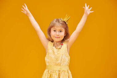 Mutlu çocukluk, mutlu çocuk duyguları. Sarı saçlı, sarı elbiseli ve altın tacı olan şirin bir prensesin portresi. Sarı stüdyo arka planı.