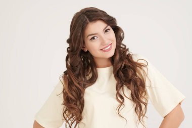 İnsanlar, mutlu duygular. Uzun kıvırcık saçlı, mutlu ve heyecanlı bir şekilde gülümseyen güzel bir kızın portresi. Beyaz stüdyo geçmişi. Kadın güzelliği.