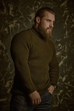 Erkeklik ve fiziksel güç kavramı. Büyük, vahşi, sakallı bir adamın portresi örgü ören bir süveter giydi..
