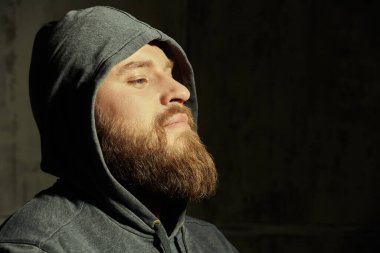 The concept of masculinity and physical strength. Male beauty. Portrait of a large brutal bearded man in a black hoodie. In the background is a concrete wall. Copy space.  clipart