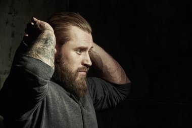 Erkeklik ve fiziksel güç kavramı. Erkek güzeli. Siyah kapüşonlu, iri yarı, sakallı bir adamın portresi. Arka planda beton bir duvar var. Boşluğu kopyala. 