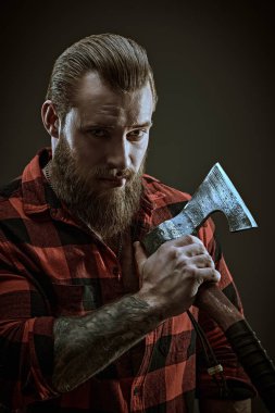 Ekose gömlekli, baltalı, vahşi sakallı bir adamın portresi. Koyu gri stüdyo geçmişi. Erkek güzelliği ve erkeklik. Berber dükkanı reklamı.