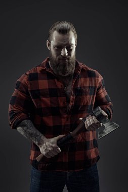 Baltayla tıraş olan ekose gömlekli vahşi sakallı bir adamın portresi. Koyu gri stüdyo geçmişi. Erkek güzelliği ve erkeklik. Berber dükkanı reklamı.