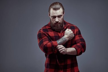 Berber dükkanı reklamı. Ekose gömlekli yakışıklı sakallı bir adamın portresi. Arka planda gri bir stüdyo ve fotokopi alanı var. Erkek güzeli. Erkeklik ve güç.