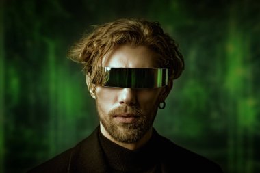 Erkek modası ve tarzı. Siyah ceketli ve tekno gözlüklü yakışıklı bir adamın portresi karanlık bir stüdyonun arka planında yeşil ışık yanıyor. Erkek saç stilleri.