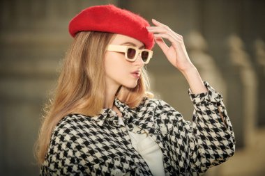 Modada zarif bir retro tarzı var. Uzun dalgalı saçlı güzel bir kadının portresi ekose ceketli, kırmızı bereli ve bej güneş gözlüklü bir şehirde poz veriyor..
