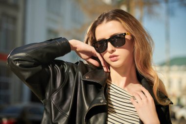 Siyah deri ceketli, siyah kot pantolonlu ve güneş gözlüklü modern bir kadın. Deri kıyafet modası. Çekici bir genç kadın. Moda ve gençlik tarzı. 
