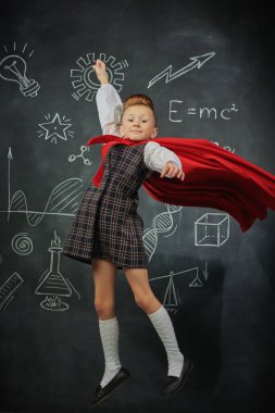 Cute little kid girl in a cloak flies like a superhero. Education and early development. Little Scientist. Background of a black chalkboard. clipart