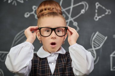 Eğitici bir kavram. Okul üniformalı, gözlüklü, kameraya şaşırmış güzel bir kızın portresi. Bilimsel çizimleri olan siyah bir kara tahta. Genç bilim adamları.