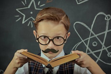Gözlüklü, bıyıklı, profesör gibi poz veren sevimli bir çocuk. Siyah bir karatahtanın arka planı. Eğitim ve erken gelişim. Genç Bilim Adamları.