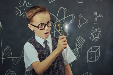 Çocukların erken gelişimi. Akıllı bir çocuk elinde yanan bir ampul tutar ve şaşırır. Tebeşirle çizilmiş siyah okul panosunun arka planı. Keşifler. Eğitim.