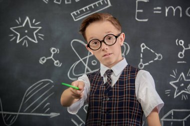 Okul üniformalı ve kameraya ciddi ciddi bakan zeki bir çocuğun portresi. Bilimsel çizimleri olan siyah bir kara tahta. Eğitim, öğretmenlik. Genç bilim adamı.