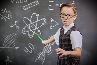 Genç bilim adamı. Okul üniformalı ve kameraya ciddi ciddi bakan zeki bir çocuğun portresi. Bilimsel çizimleri olan siyah bir kara tahta. Eğitim.