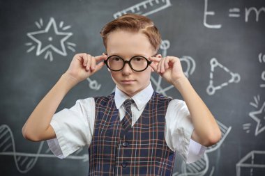 Okul üniformalı ve gözlüklü bir çocuğun kameraya ciddi ciddi baktığı bir fotoğraf. Bilimsel çizimleri olan siyah bir kara tahta. Eğitim. Genç bilim adamları.
