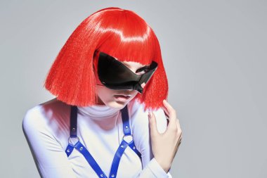 Parlak kırmızı makyajlı, kızıl saçlı, fütüristik aynalı gözlüklü ve beyaz tulumlu siber punk kızı. Gri stüdyo geçmişi. Sanal oyunlar. Makyaj ve saç stili. 