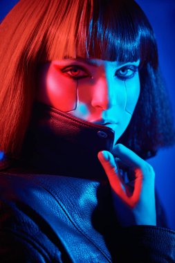 Siber punk konsepti. Parlak kırmızı makyajlı, kızıl saçlı, siyah ışıkta poz veren güzel bir siber punk kızı portresi. Sanal oyunlar. Makyaj ve saç stili. 