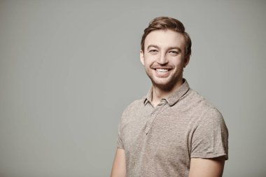 Polo tişört giyen ve kameraya gülümseyen orta yaşlı bir adamın portresi. İnsanlar, duygular. Erkek sağlığı ve güzelliği. Fotokopi alanı olan gri bir arkaplanda stüdyo resmi. 