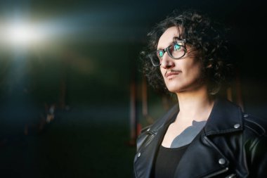 Gayri resmi hippi. Esmer, kıvırcık saçlı, gözlüklü, siyah deri ceketli, vücudunda dövmeler olan bir adamın portresi..