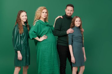 Güzel mutlu anne ve baba ve sevgili kızları yeşil bir stüdyo arka planında birlikte poz veriyorlar. Mutlu ve dost canlısı bir ailenin portresi..