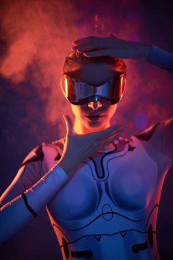 Fütürist gözlüklü güzel bir siber kızın portresi ateşin yansımalarının arka planında duruyor, kızgın ışınlar. Kozmik stil. Siber uzay, sanal gerçeklik oyunları.