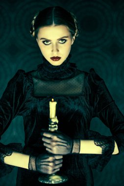 Zarif siyah kadife elbise ve dantel eldivenli dramatik bir esmer kızın portresi, gecenin karanlığında elinde mumla dikiliyor. Gotik roman, mistisizm..