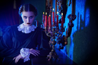 Gotik roman. Katı siyah elbiseli, beyaz yakalı esmer ciddi bir kız geceleri kasvetli bir malikanede şöminenin yanında duruyor. Addams Ailesi.