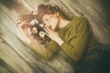 Bahar ve yaz havası. Dalgalı saçlı, tahta bir zeminde uzanmış, saçlarında beyaz çiçeklerle güzel bir kız. Doğal kozmetikler. Kadın güzelliği ve moda. Boşluğu kopyala. 