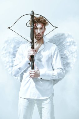 Sevgililer Günü. Savaşçı yakışıklı bir adam, Aşk Tanrısı yüzünde yaralar olan Aşk Tanrısı, kurbanına bir ok atmak niyetinde. Fantezi. Stüdyo beyaz arkaplan.