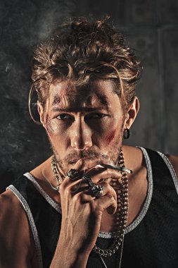 Kötü adam konsepti. Yüzünde morluklar ve yaralar olan, beton duvarlarla karanlık bir odada sigara içen sert bir erkek haydudun portresi. Aksiyon filmi kahramanı.
