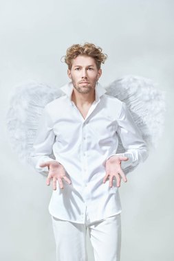 Beyaz elbiseli ve beyaz kanatlı cesur, yakışıklı bir aşk meleği. Beyaz arka plan. Aşk Tanrısı Aşk Tanrısı. Sevgililer Günü.