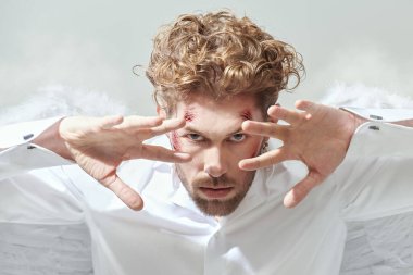 Fantezi kahramanı aşığı. Beyaz elbiseli, beyaz kanatlı, yüzünde yaraları olan çekici bir aşk meleği kameraya bakıyor. Aşk Tanrısı Aşk Tanrısı. Sevgililer Günü.